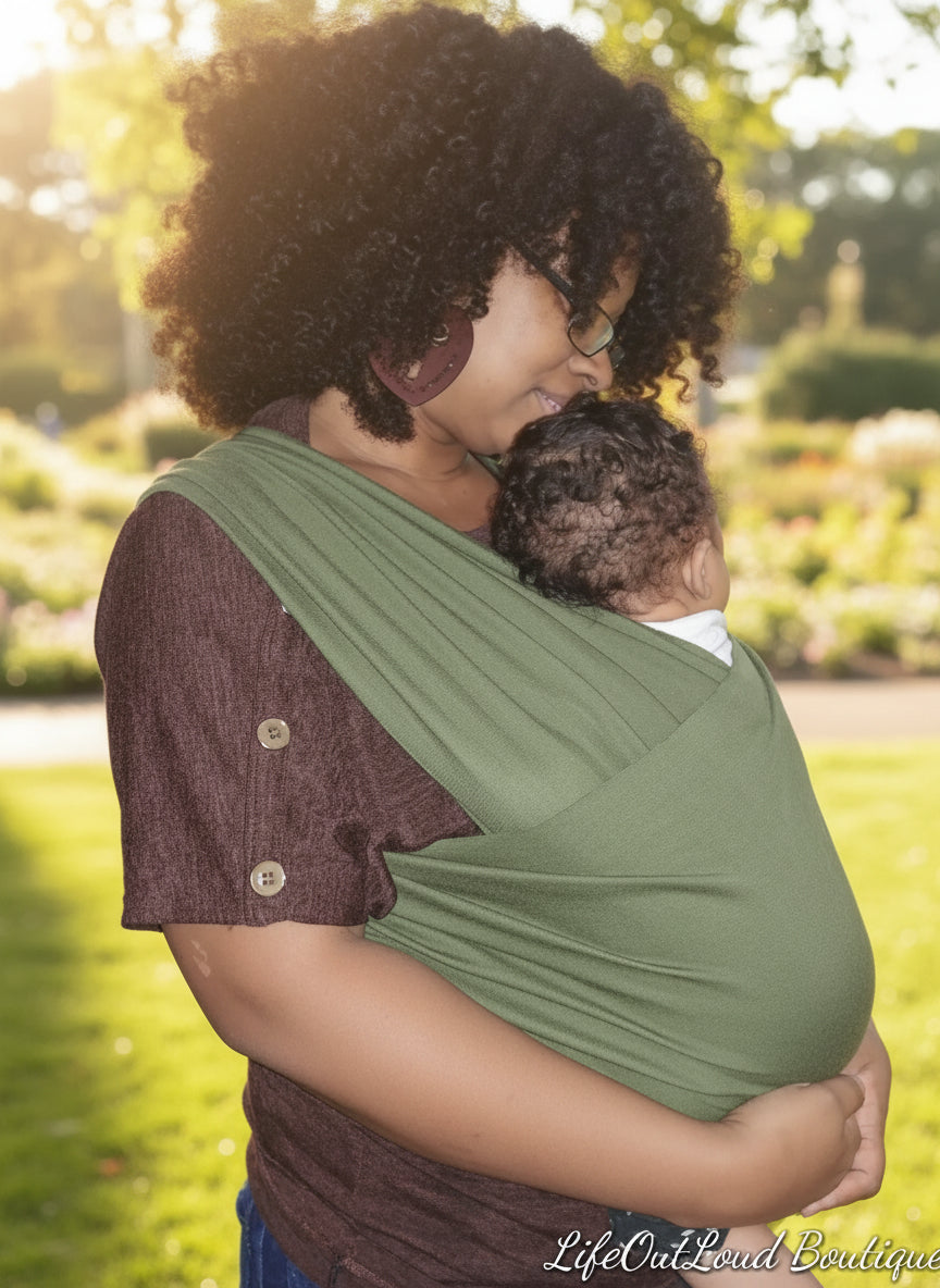 Woman holding a child in a green sling against a plain background
